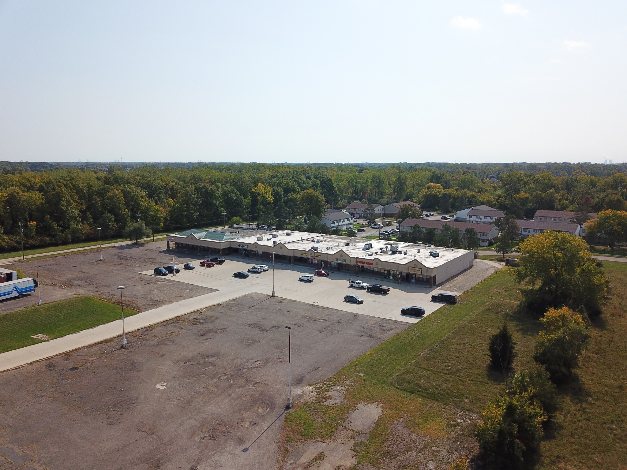 Earlier aerial view of a retail center with large unpaved parking areas and fewer occupied storefronts
